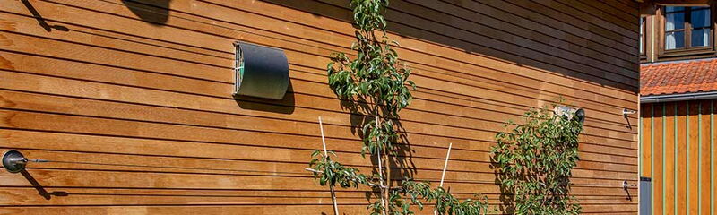 Eine Holzfassade mit Pflanzen und Lüftungsöffnungen, die ein modernes, nachhaltiges Design zeigt.