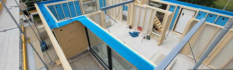 Blick auf den Rohbau eines Hauses mit blauen Elementen und Holzrahmen auf der Baustelle.