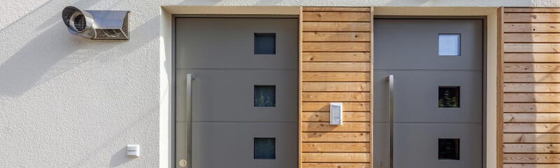 Zwei moderne Eingangstüren mit den Hausnummern 13 und 13a, umgeben von Holz- und Putzfassade.