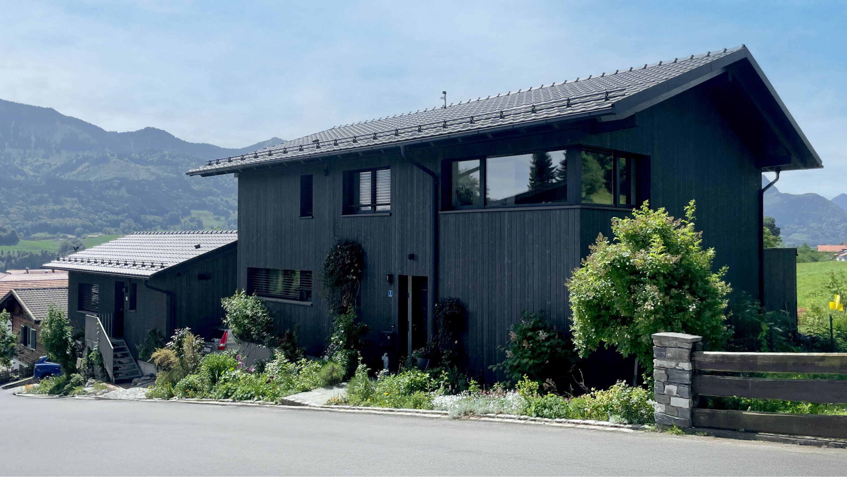 Dieses ist die Umsetzung des Architektenentwurfs eines Einfamilienhauses mit Ferienwohnung am Samerberg. Besonderheit ist die dunkelgraue Holzverschalung und die großen Fenster auf der Südseite.