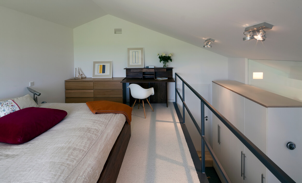 Ein modernes, helles Schlafzimmer im Passivhaus Chieming mit einem gemütlichen Bett und einem Schreibtisch unter der Dachschräge.