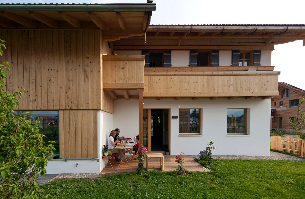 Eine Familie sitzt am Tisch vor einem modernen Passivhaus in Chieming und genießt eine Mahlzeit im Freien.