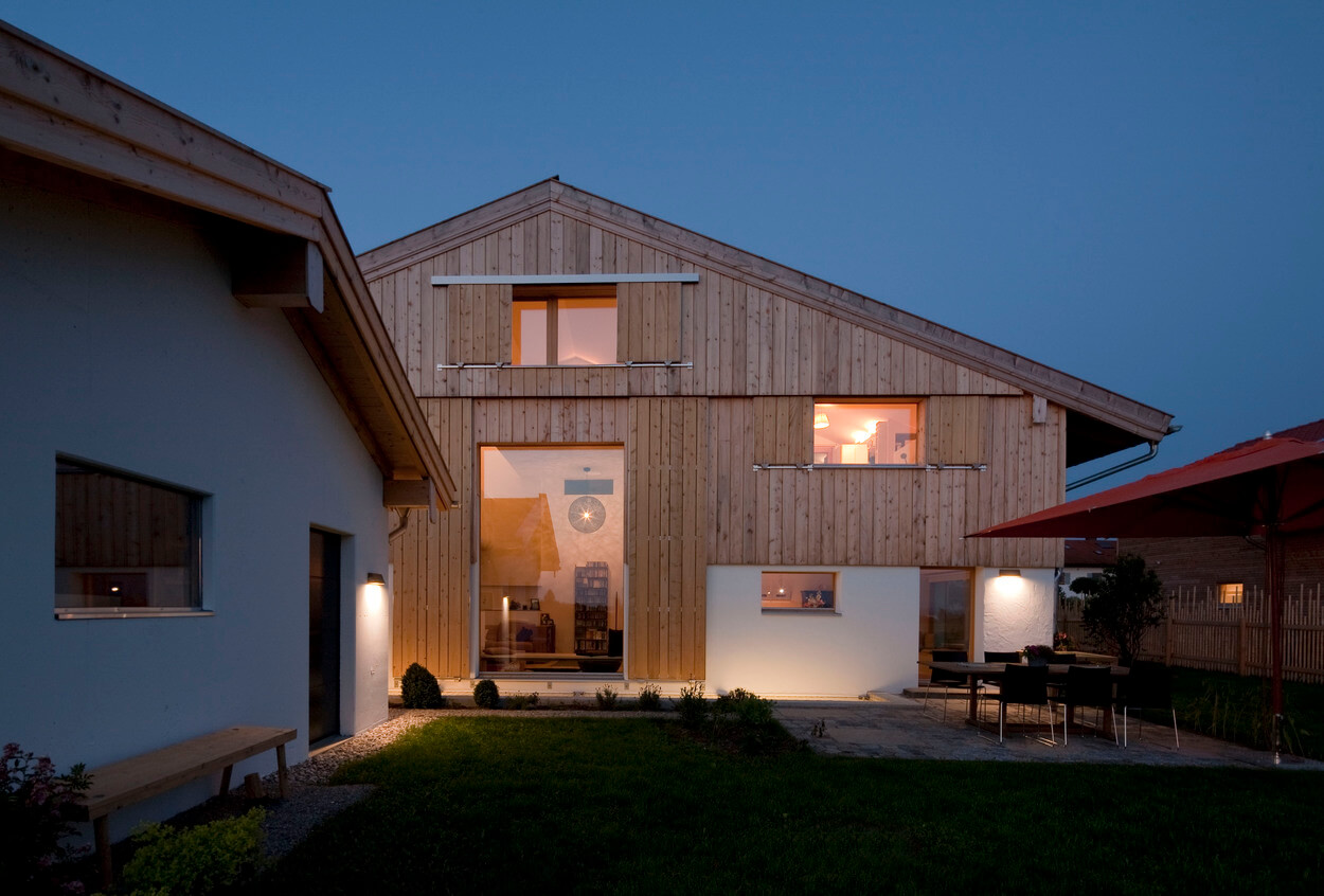 Ein modernes Passivhaus in Chieming leuchtet abends mit warmem Licht, umgeben von einem gepflegten Garten.