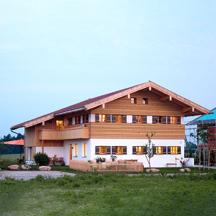 Ein modernes Passivhaus in Chieming mit Holzverkleidung und großen Fenstern steht in einer grünen Landschaft.