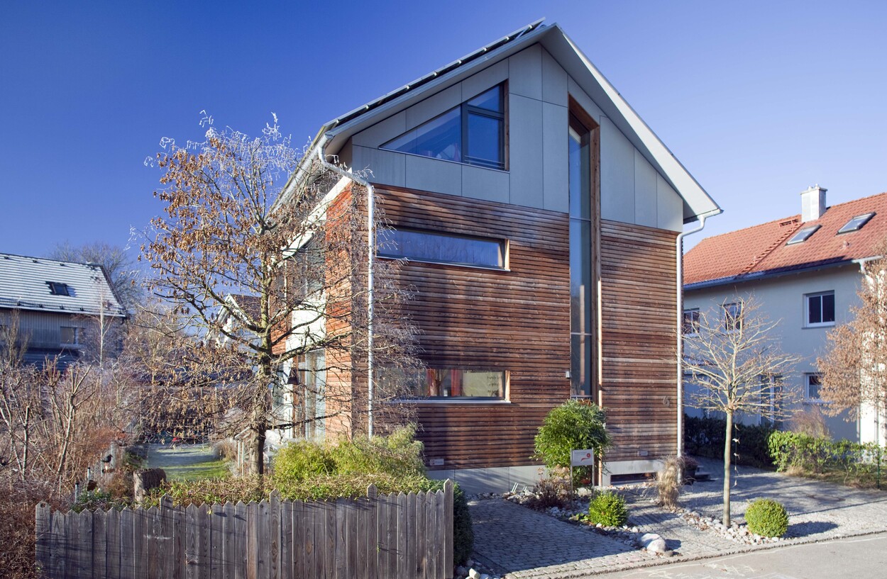 Ein modernes Passivhaus in Fürstenfeldbruck mit Holzfassade und gepflegtem Vorgarten an einem sonnigen Tag.