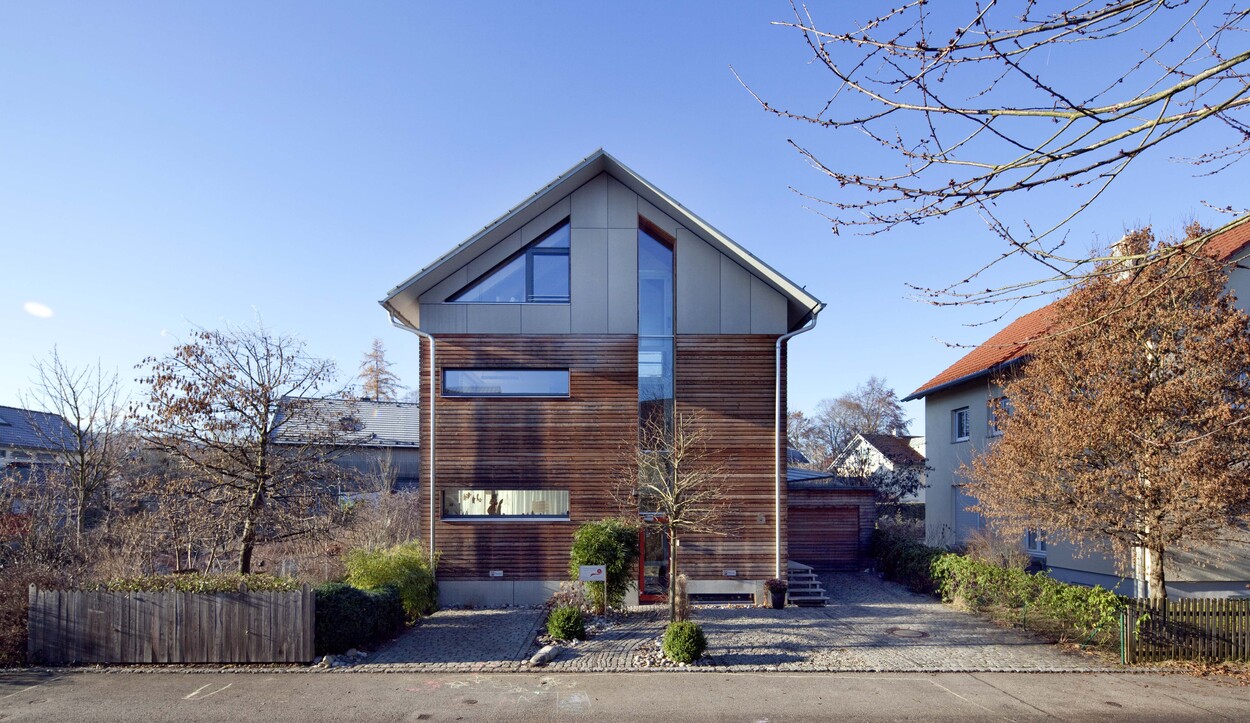 Ein modernes Passivhaus mit Holzfassade steht an einem sonnigen Tag in einem ruhigen Wohngebiet in Fürstenfeldbruck.