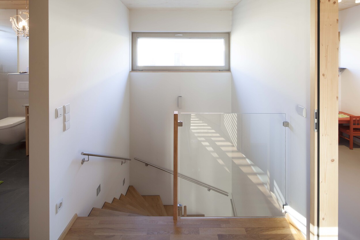 Eine moderne Treppe in einem Passivhaus in Fürstenfeldbruck mit Glasgeländer und hellem Holz führt ins Obergeschoss.