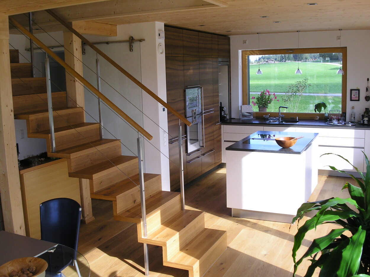 Ein modernes Passivhaus in Breitbrunn zeigt eine helle Küche mit Holztreppe und großem Fenster zum Garten.