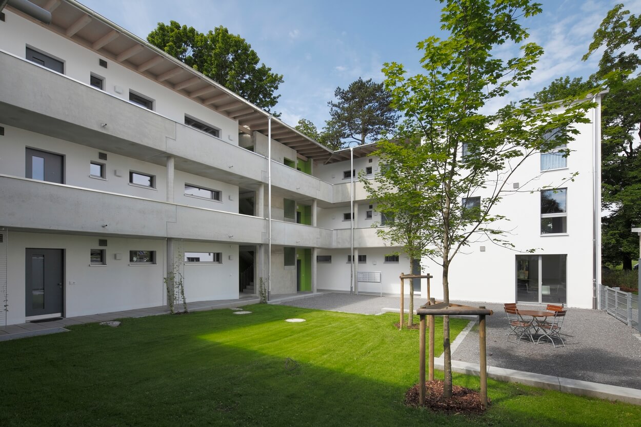 Ein modernes Passivhaus mit weißer Fassade und Balkonen liegt idyllisch im Grünen des Koribiansparks in Heufeld.