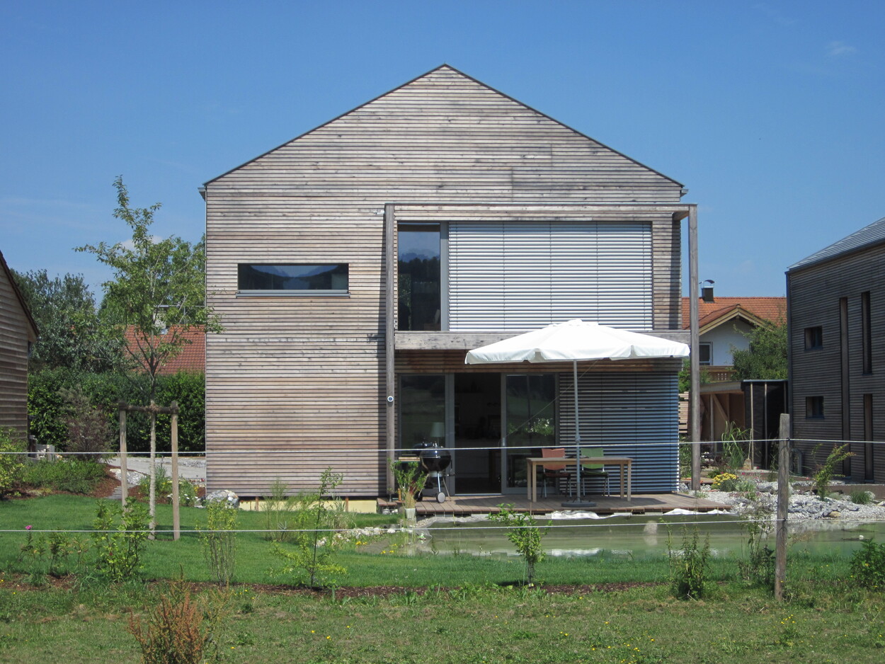 Ein modernes Passivhaus in Thalham mit Holzverkleidung und Terrasse steht bei sonnigem Wetter in einem gepflegten Garten.