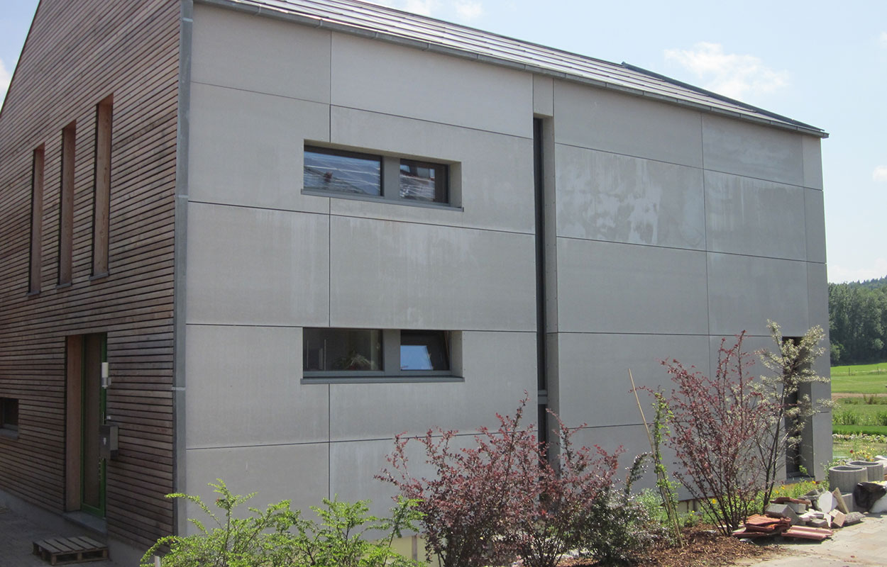 Ein modernes Passivhaus in Thalham mit Holz- und Putzfassade steht inmitten einer grünen Landschaft unter blauem Himmel.