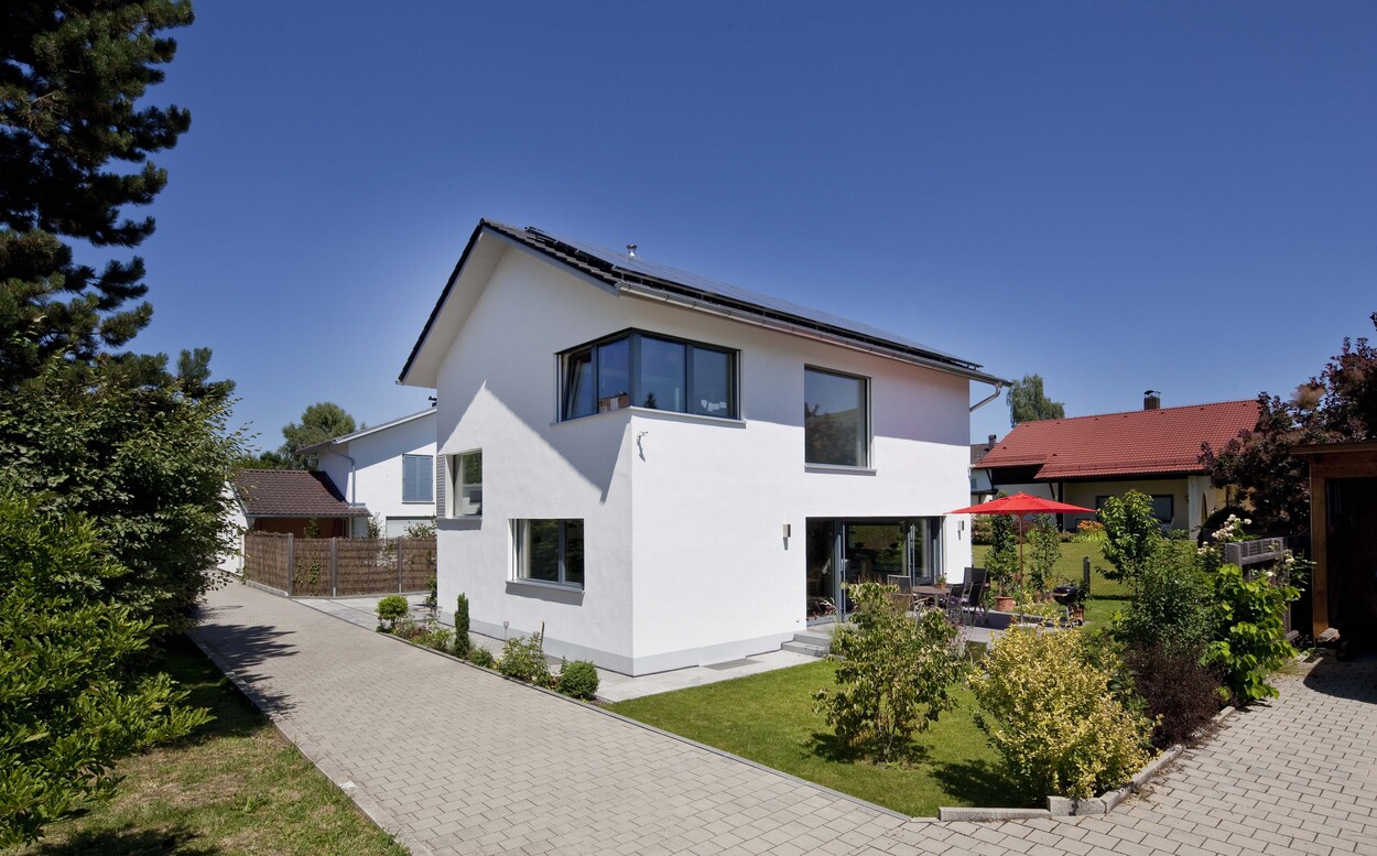 Ein modernes Passivhaus in Bad Aibling mit gepflegtem Garten und Terrasse unter strahlend blauem Himmel.