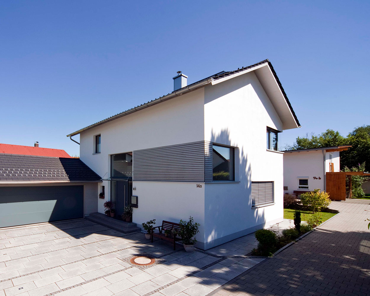 Ein modernes Passivhaus in Bad Aibling steht unter klarem Himmel und ist von einem gepflegten Garten umgeben.