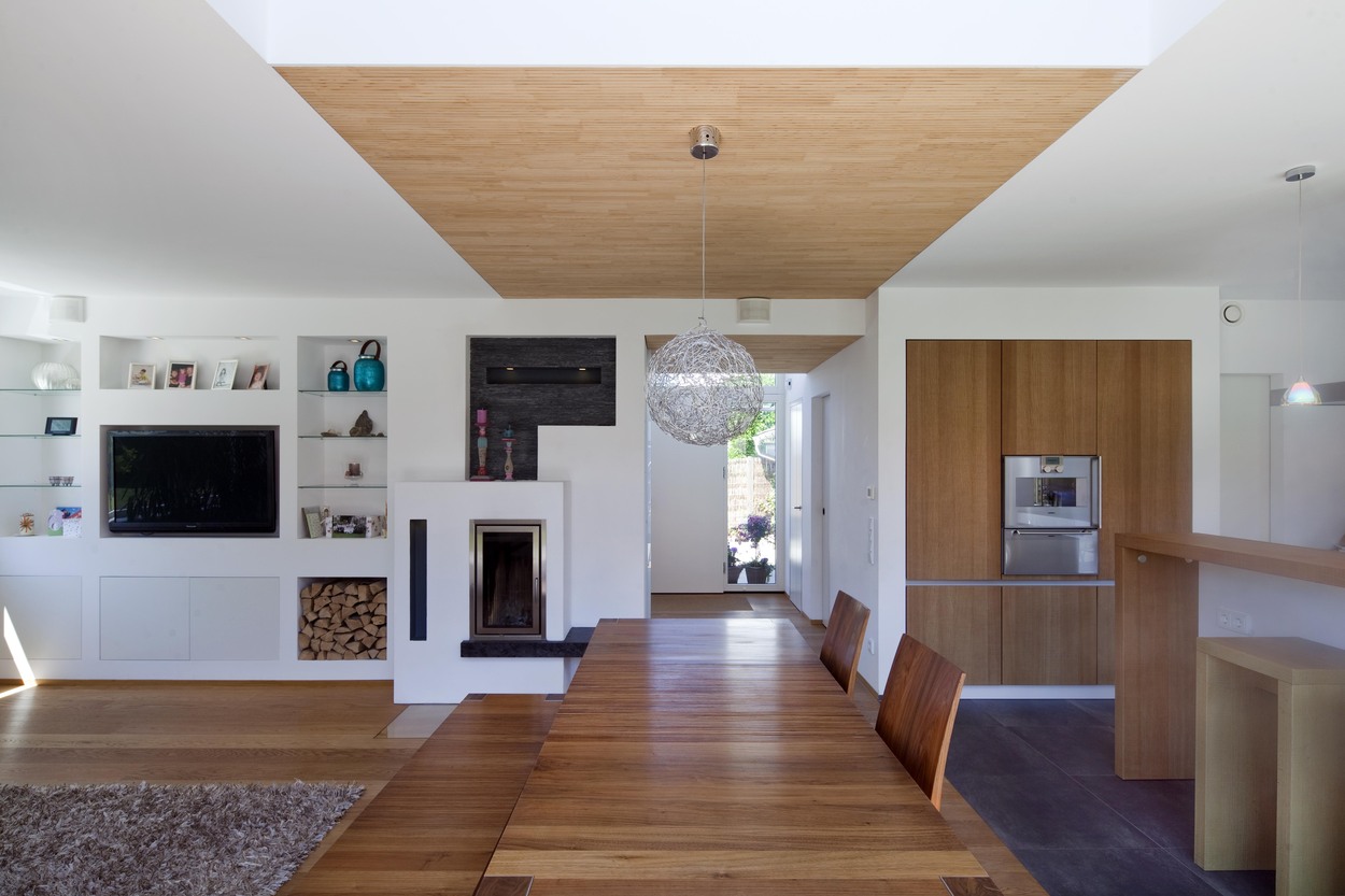 Ein stilvolles Esszimmer in einem modernen Passivhaus in Bad Aibling mit Holzmöbeln, elegantem Kamin und raffinierter Beleuchtung.