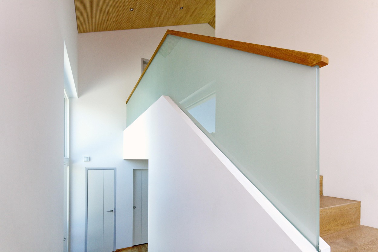 Eine moderne Treppe mit Glasgeländer und Holzdetails in einem Passivhaus in Bad Aibling betont das energieeffiziente Design.