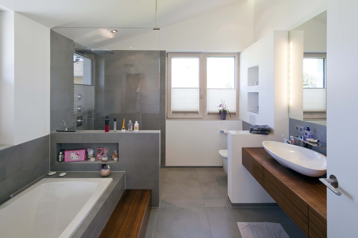 Ein modernes Badezimmer in einem Passivhaus in Bad Aibling mit Badewanne, Holzdetails und großen Fenstern.