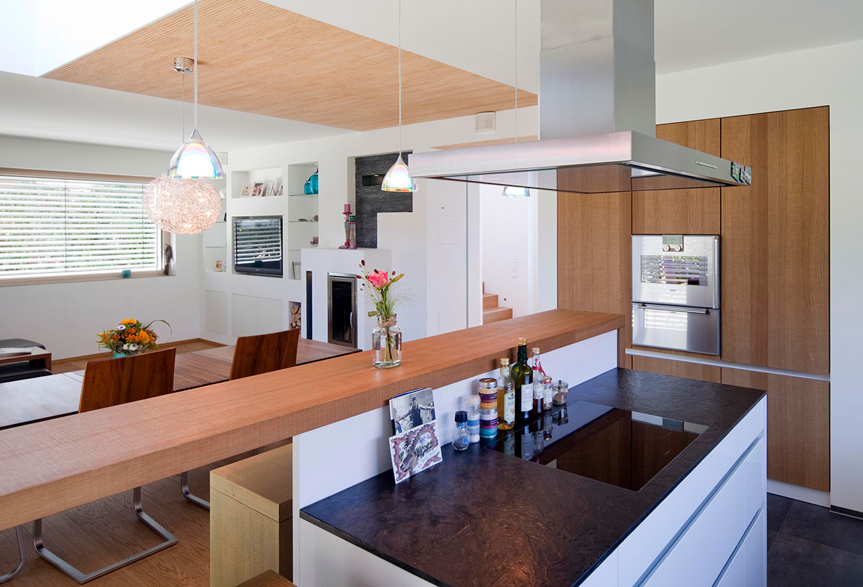 Moderne Küche im Passivhaus in Bad Aibling mit Holzverkleidung, stilvoller Beleuchtung und eleganter Kochinsel.