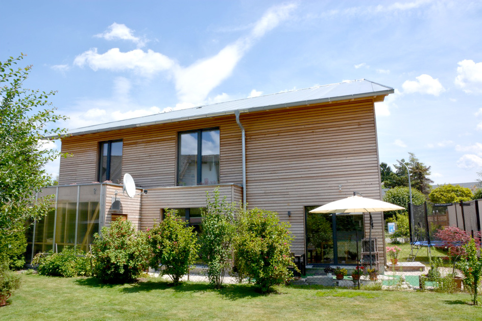 Ein modernes Passivhaus in München mit Holzfassade erstrahlt im Sonnenlicht, umgeben von einem gepflegten Garten.