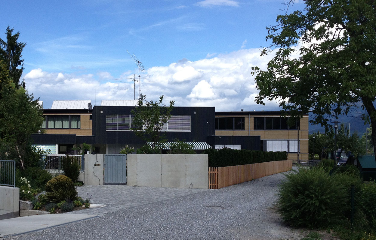 Ein modernes Passivhaus in Brannenburg beeindruckt mit auffälliger Architektur und gepflegtem Garten unter klarem Himmel.
