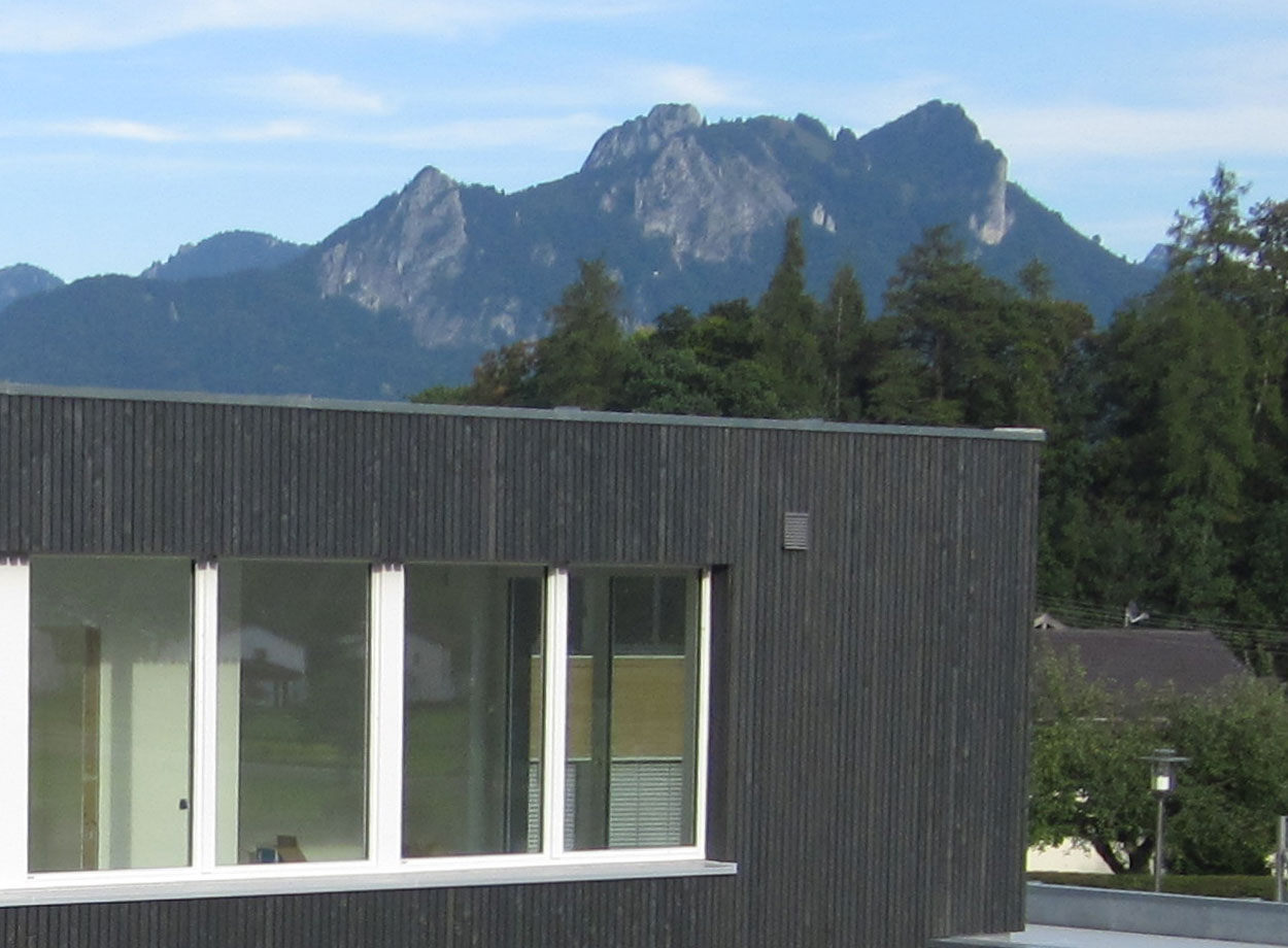 Ein modernes Passivhaus in Brannenburg zeigt große Fenster vor der Kulisse beeindruckender Berge.