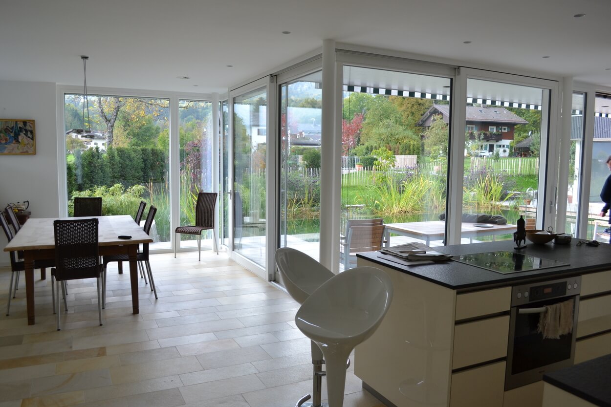 Ein modernes Passivhaus in Brannenburg bietet eine offene Küche mit großen Fenstern und Blick auf den grünen Garten.