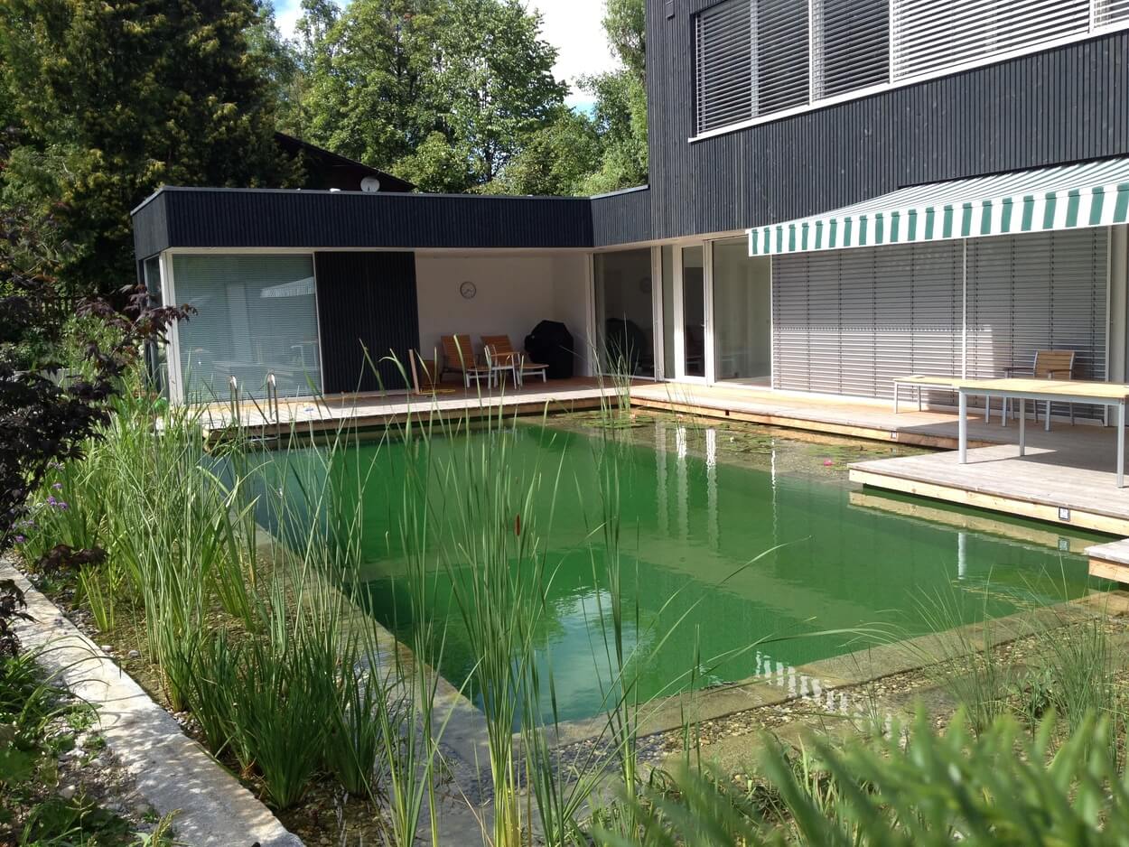 Ein modernes Passivhaus in Brannenburg mit einem natürlichen Teich und einem Terrassenbereich im Grünen.