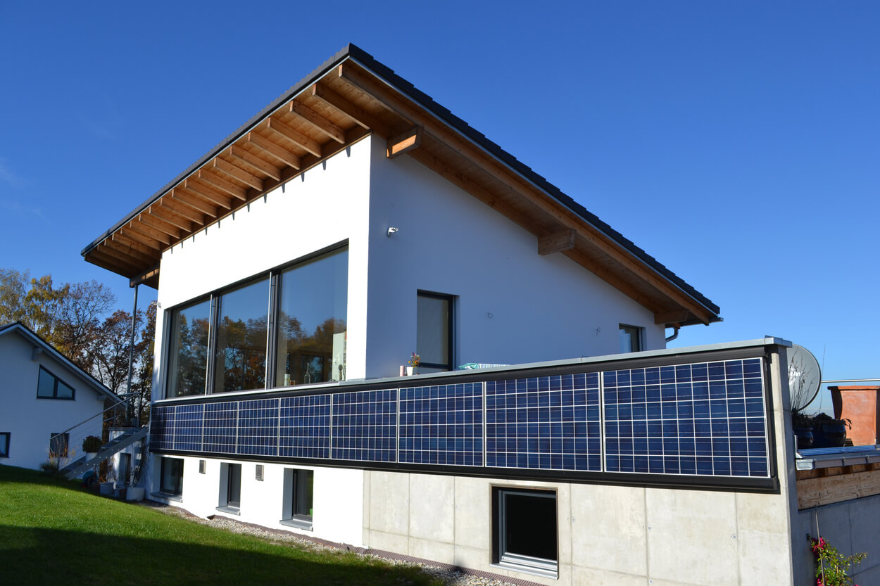 Ein modernes Passivhaus in Soyen mit großen Fenstern und Solarpaneelen glänzt unter einem klaren, blauen Himmel.
