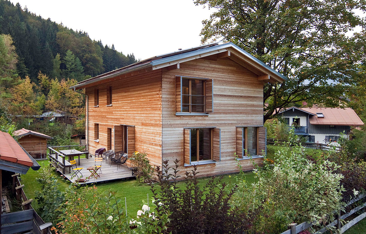 Ein modernes Holzhaus in Schliersee steht idyllisch von üppigem Grün umgeben, mit einer einladenden Terrasse.