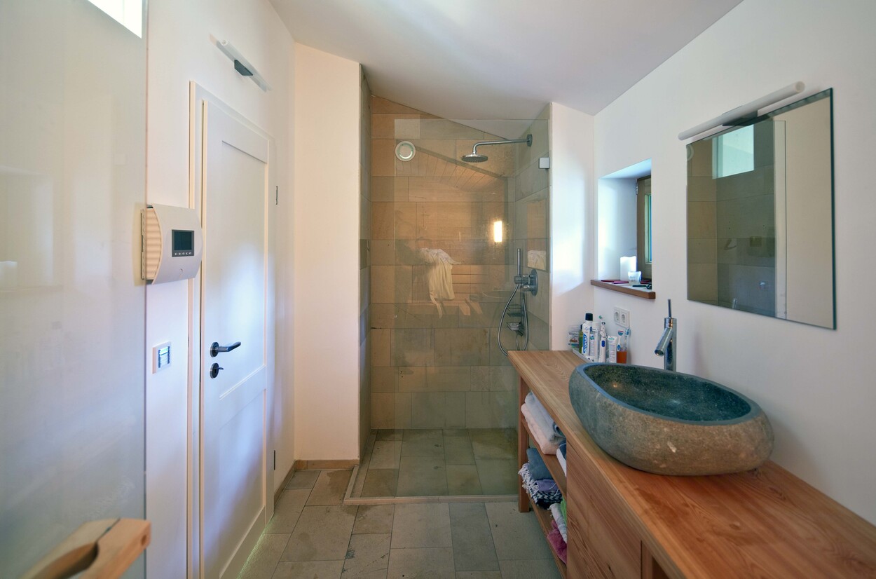 Ein modernes Badezimmer im Holzhaus am Schliersee mit Steinwaschbecken und großer, begehbarer Dusche.