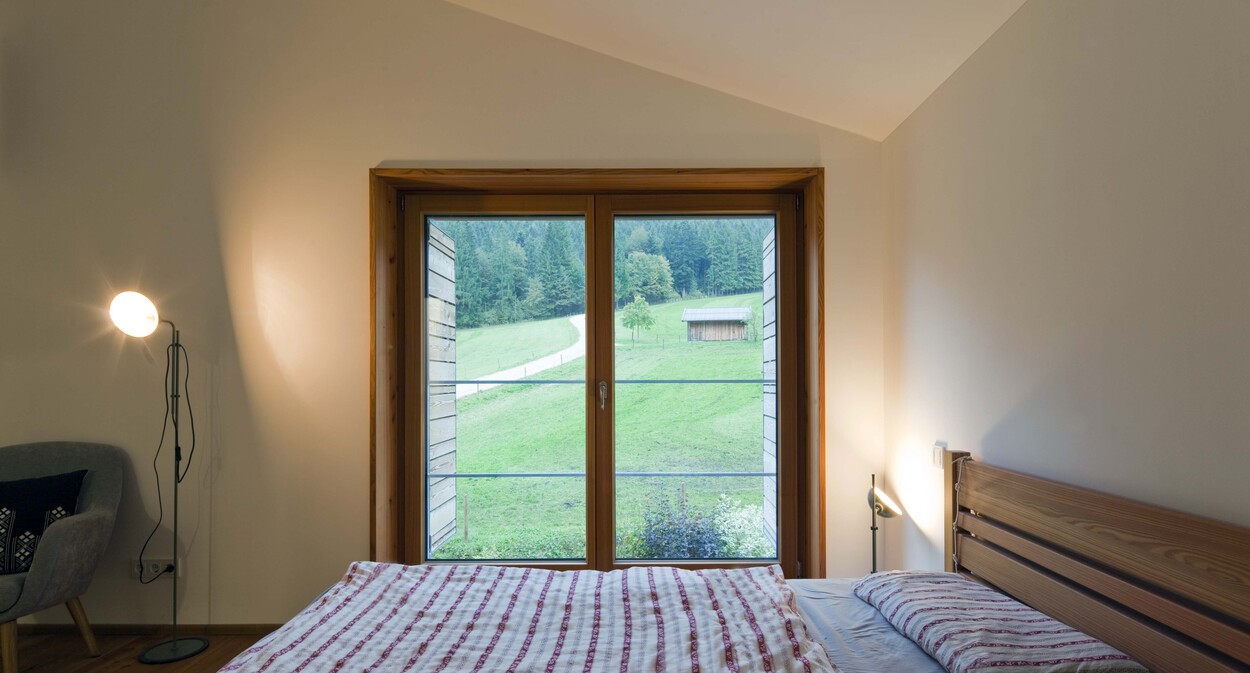 Ein gemütliches Schlafzimmer im Holzhaus bietet einen idyllischen Blick auf eine grüne Wiese und ein kleines Haus am Schliersee.