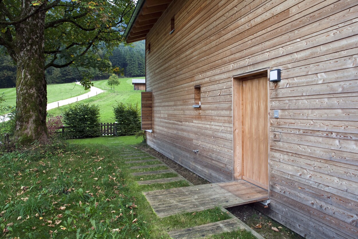 Ein modernes Holzhaus mit Eingangstür steht idyllisch in einer grünen Landschaft nahe Schliersee.