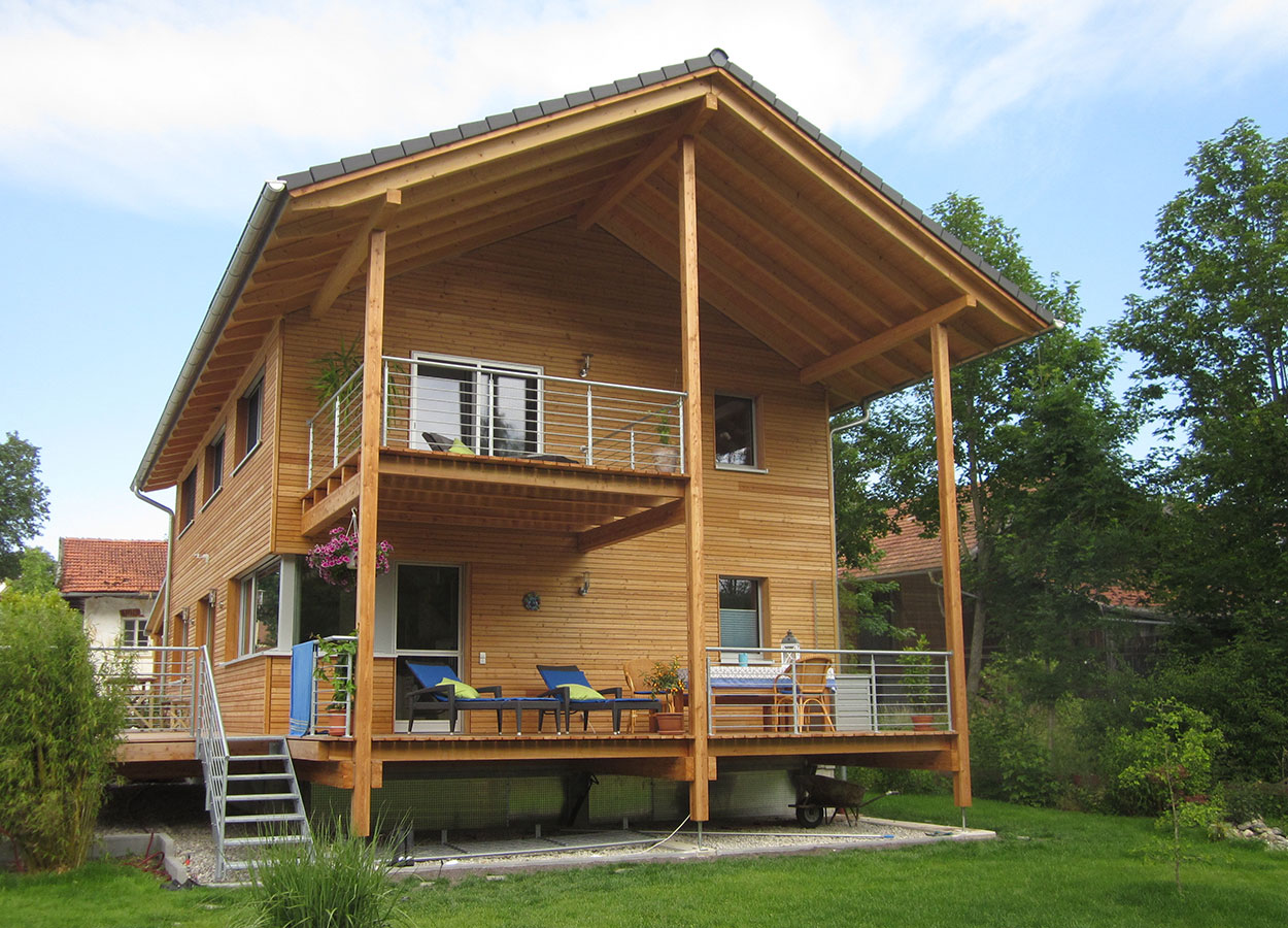 Ein modernes Holz-Passivhaus in Glonn mit großen Terrassen, eingebettet in grüne Natur und strahlendem Sonnenschein.