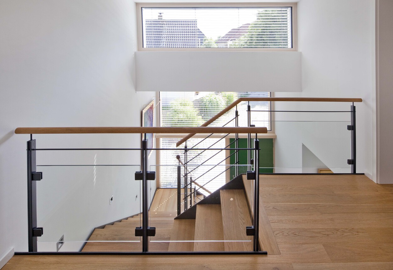 Ein modernes Treppenhaus in einem Passivhaus in Ismaning, durchflutet von natürlichem Licht, zeigt ein elegantes Holzgeländer.