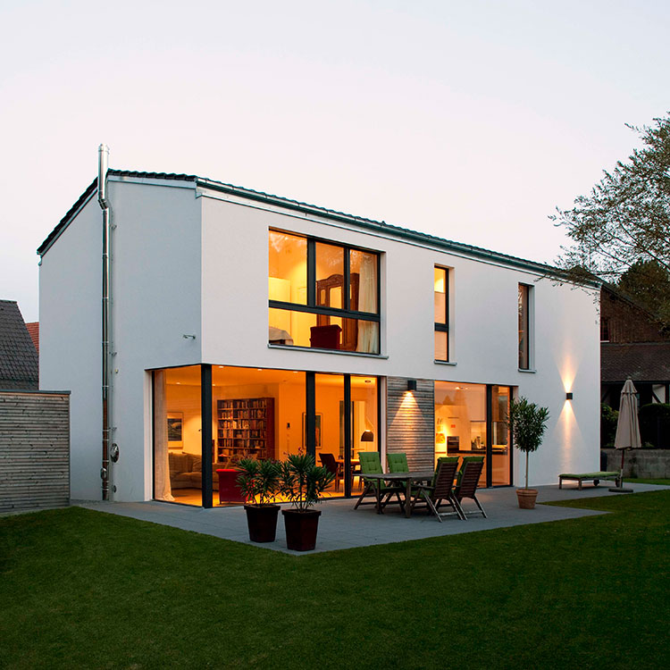 Ein modernes Passivhaus in Ismaning mit großen Glasfronten und beleuchteter Terrasse erstrahlt bei Abenddämmerung.