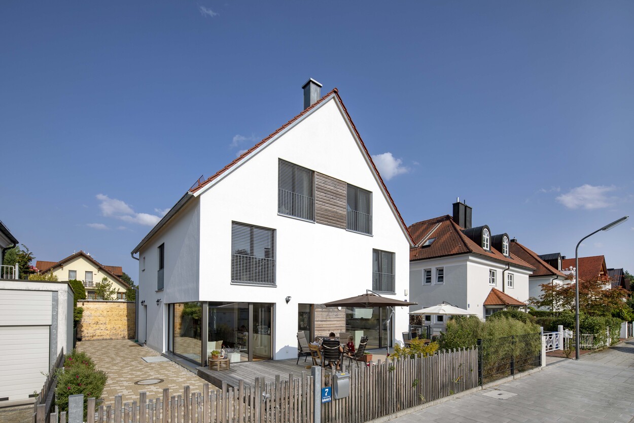 Ein modernes Doppelhaus in München steht unter klarem Himmel, mit Terrasse und gepflegtem Garten im Vordergrund.