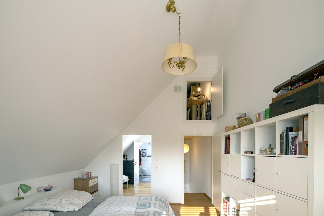 Ein modernes Schlafzimmer in einem Münchner Doppelhaus zeigt eine stilvolle Einrichtung mit schräger Decke und Regalen.