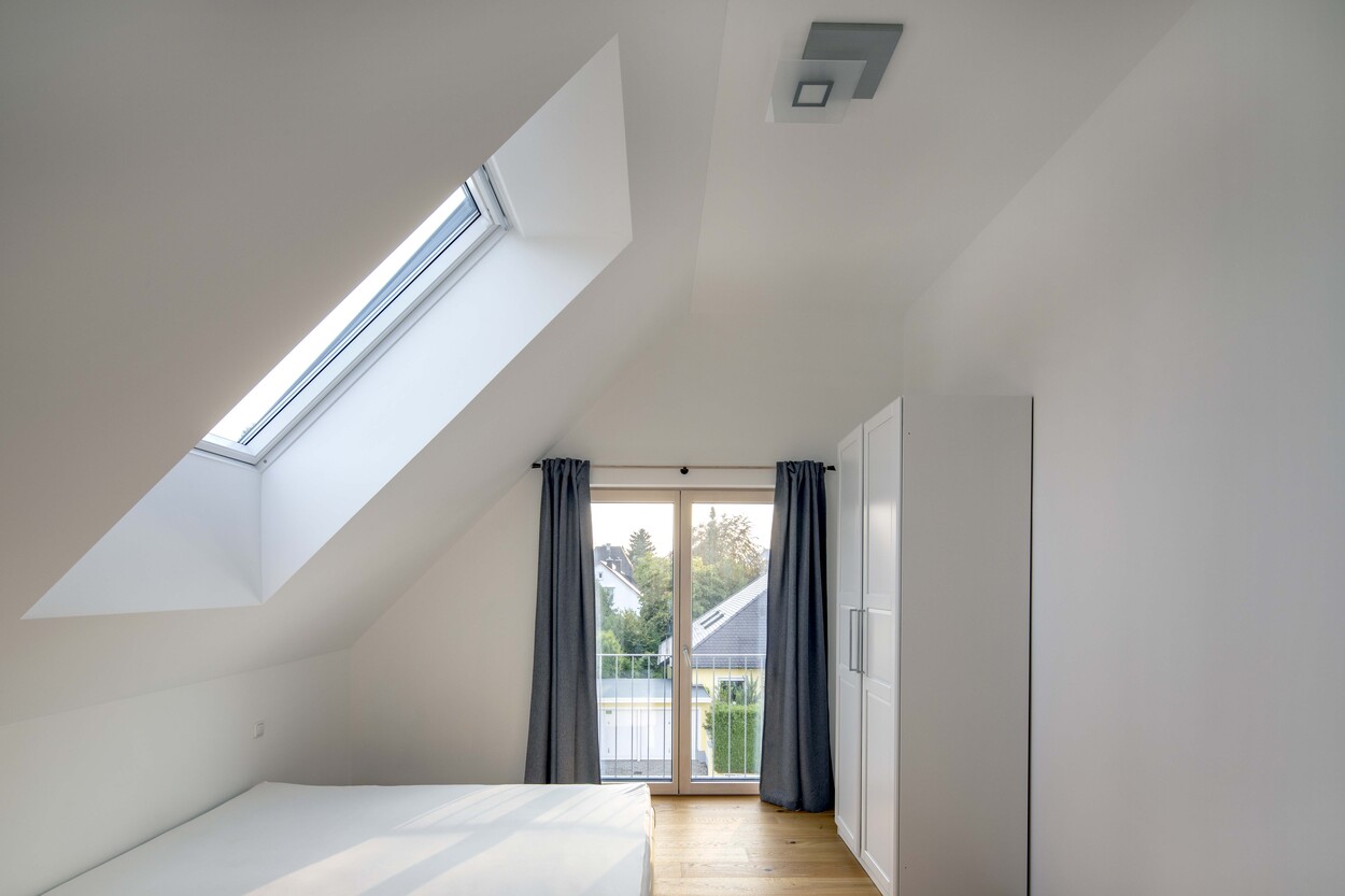 Ein modernes Schlafzimmer in München mit Dachfenster und Balkon bietet viel Tageslicht und einen Blick ins Grüne.