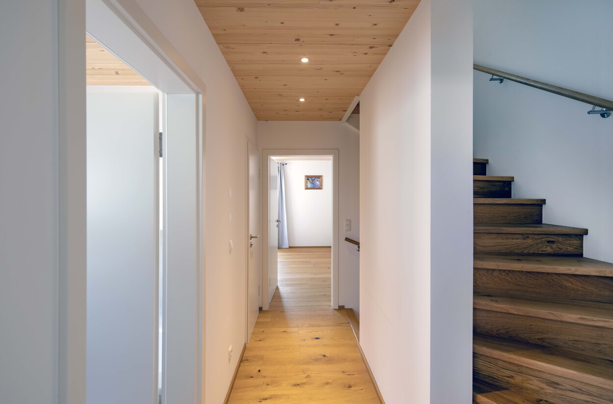 Ein moderner Flur in einem Münchner Doppelhaus zeigt elegante Holztreppen und Türen zu benachbarten Räumen.