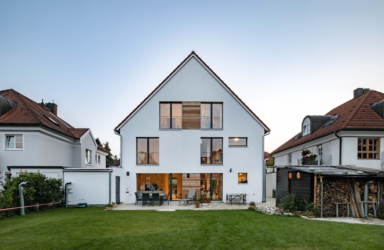 Eine moderne Doppelhaushälfte in München mit großen Fenstern und gepflegtem Garten strahlt im Licht des Sonnenuntergangs.