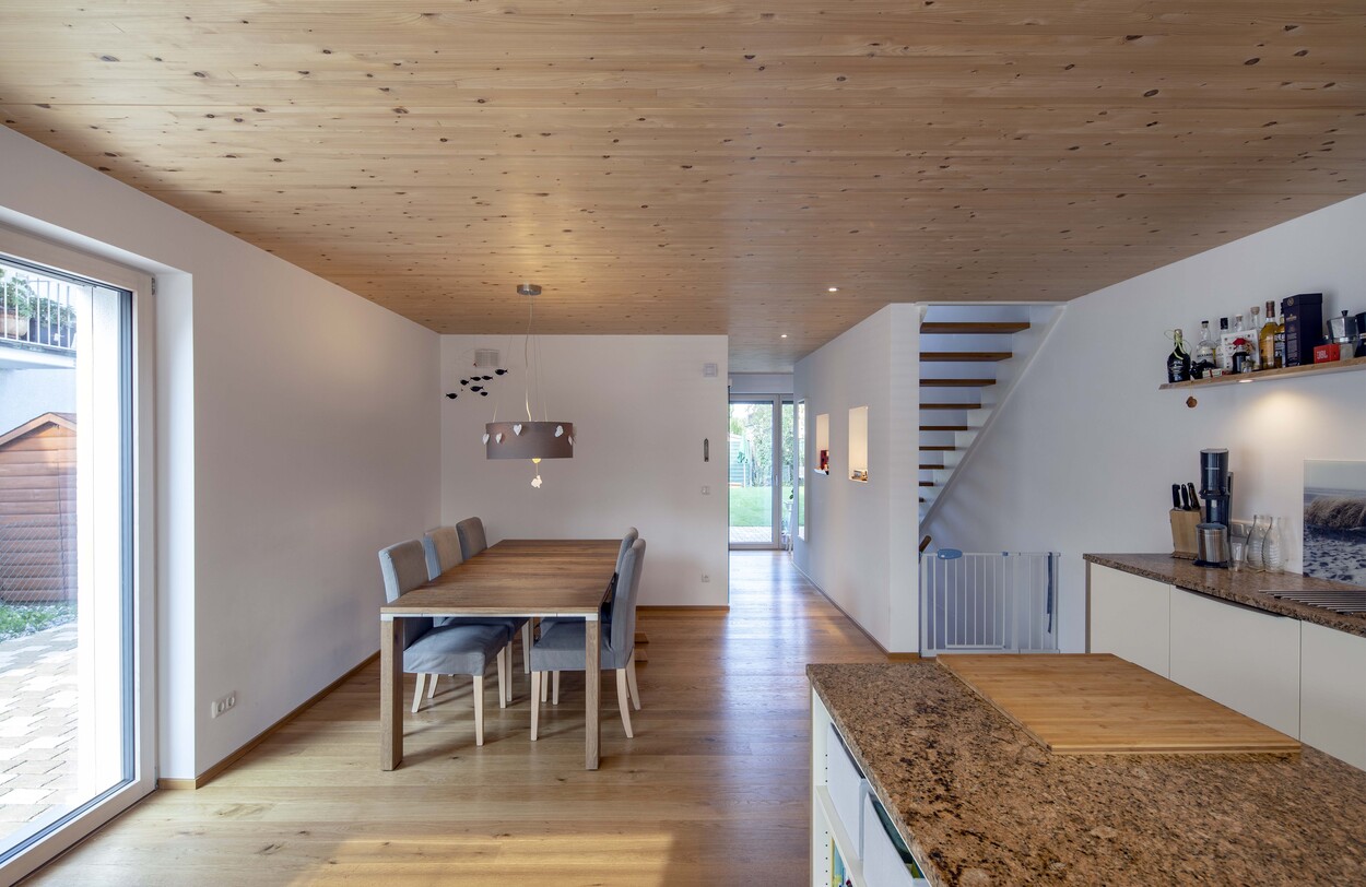 Ein modernes Esszimmer in einem Münchner Doppelhaus mit Holzböden, einem Esstisch und offener Küche.