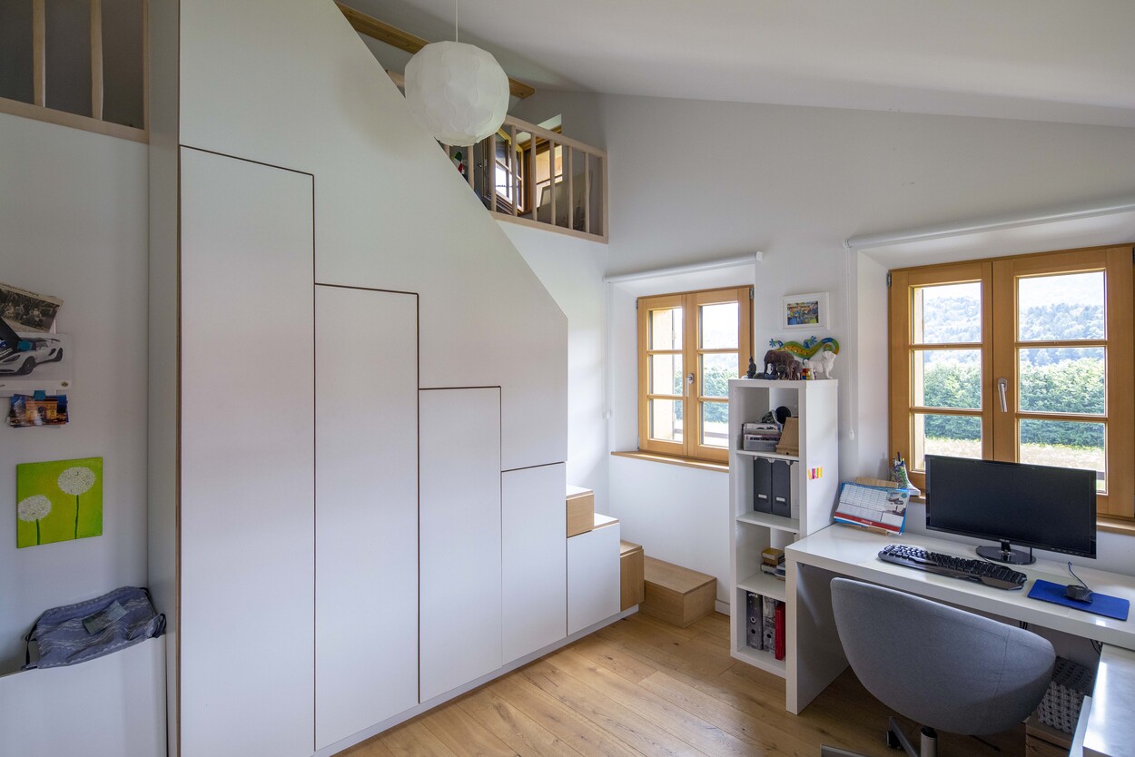 Ein modernes Arbeitszimmer in einem Holzhaus in Schleching mit Schreibtisch, Regalen und großen Fenstern.