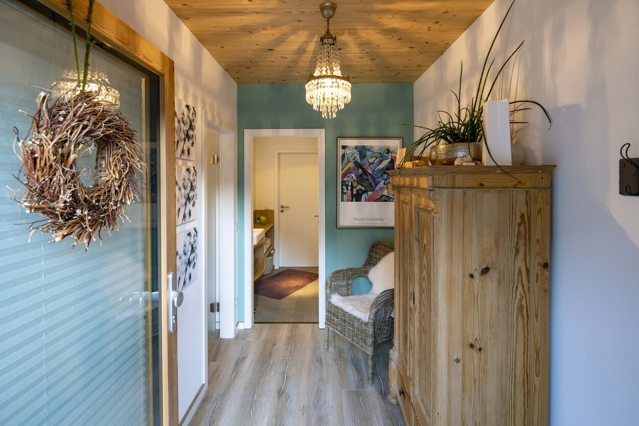 Ein einladender Flur in einem Holzhäuschen mit rustikalem Schrank, geflochtenem Sessel und dekorativem Kranz an der Tür.