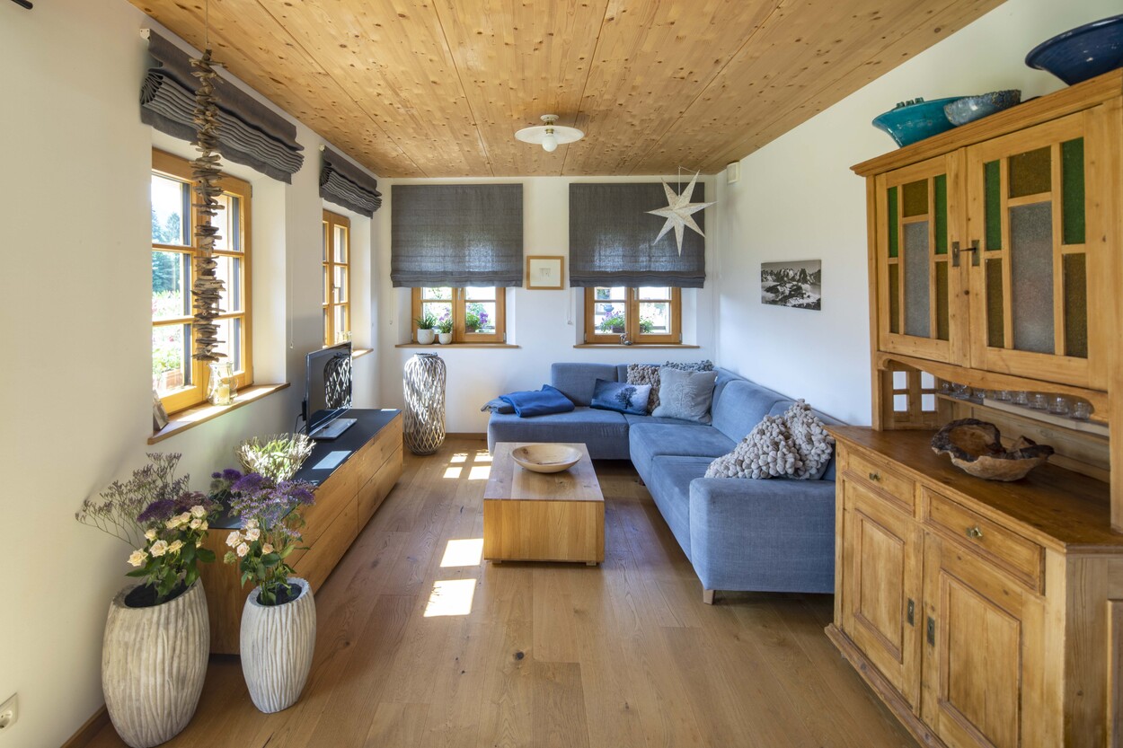 Ein gemütliches Wohnzimmer in einem Holzhaus in Schleching mit blauer Couch, Holzmöbeln und dekorativen Blumenvasen.
