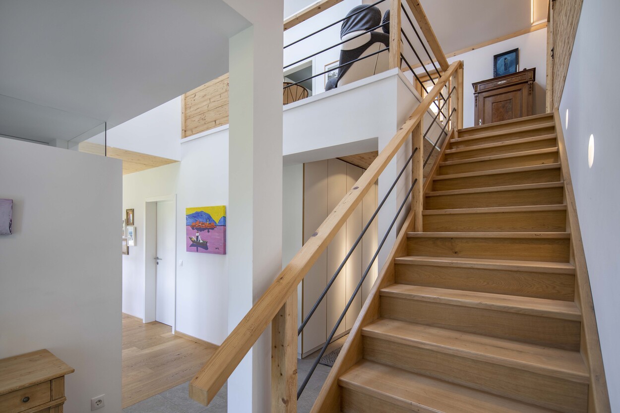 Eine moderne Holztreppe führt in einem hellen, offenen Wohnraum eines Hauses in Schleching nach oben.