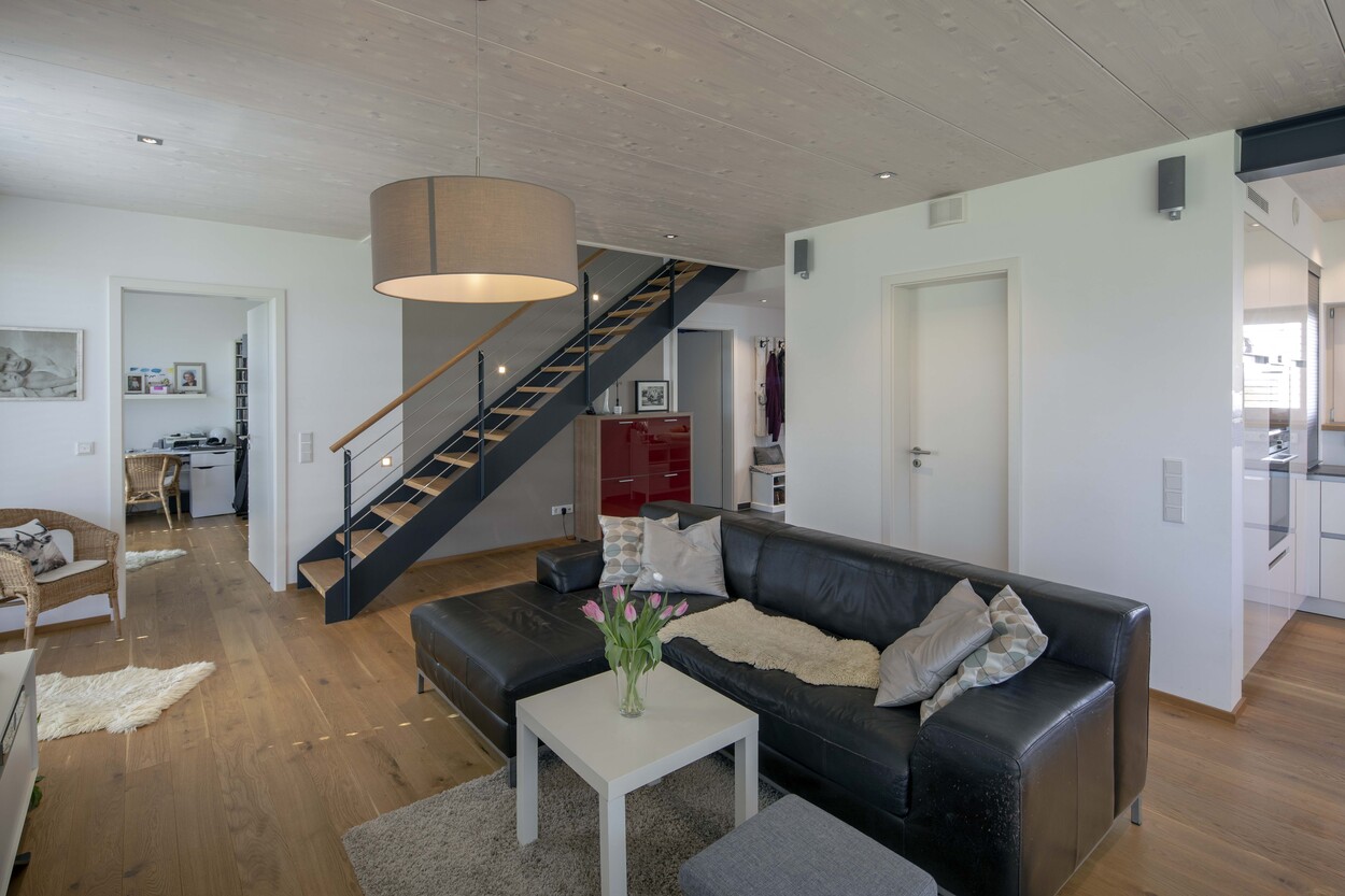 Ein modernes Wohnzimmer in Tuntenhausen mit schwarzem Ledersofa und Tulpen auf dem Tisch in einem Niedrigenergiehaus.