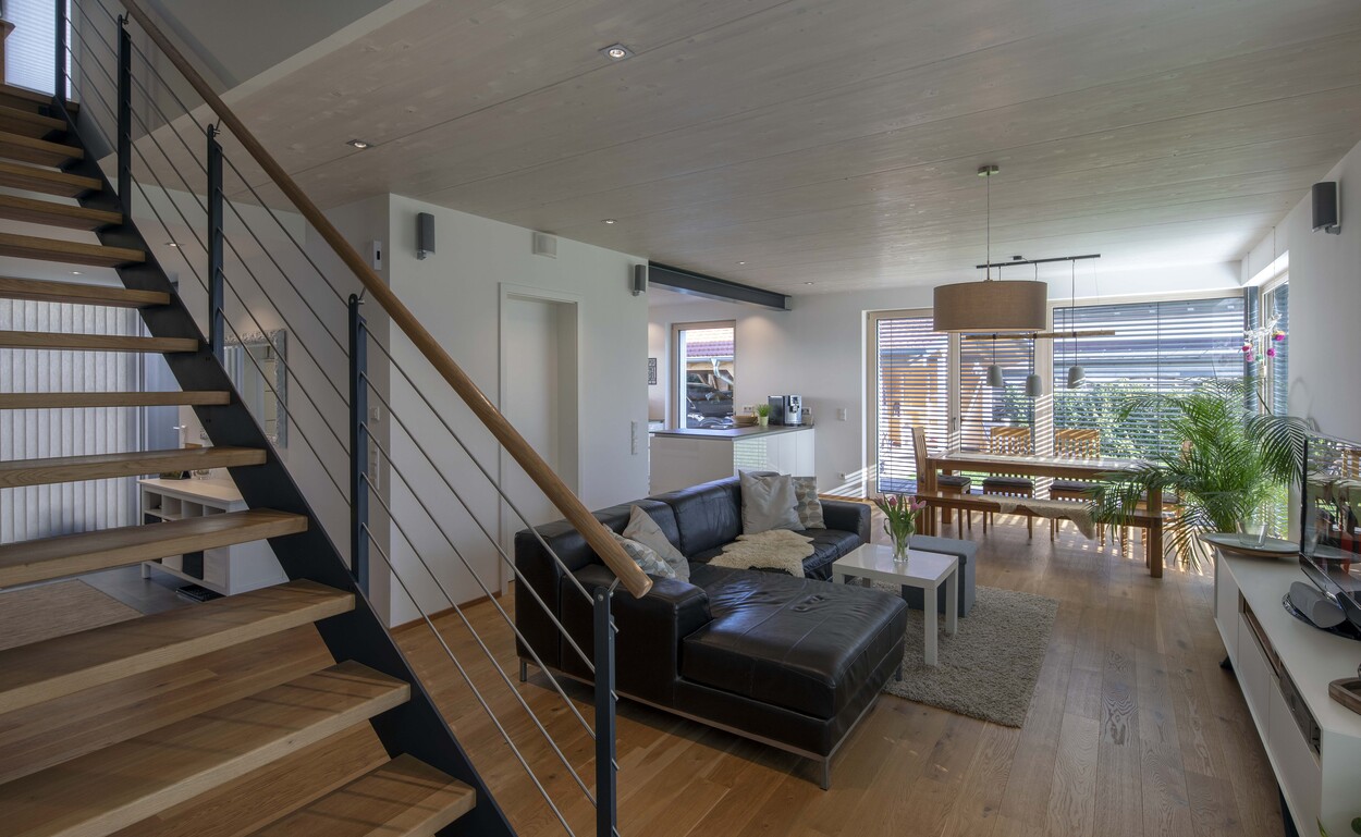 Ein helles Wohnzimmer im modernen Niedrigenergiehaus in Tuntenhausen mit Holztreppe, Ledersofa und stilvollem Esstisch.