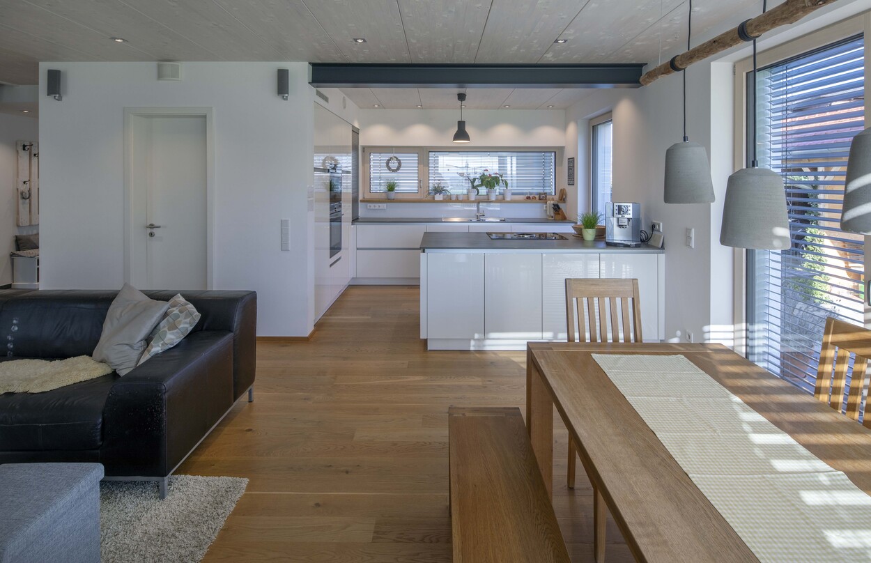 Das Wohnzimmer eines Niedrigenergiehauses in Tuntenhausen zeigt eine moderne Küche und einen Esstisch aus Holz im Licht.