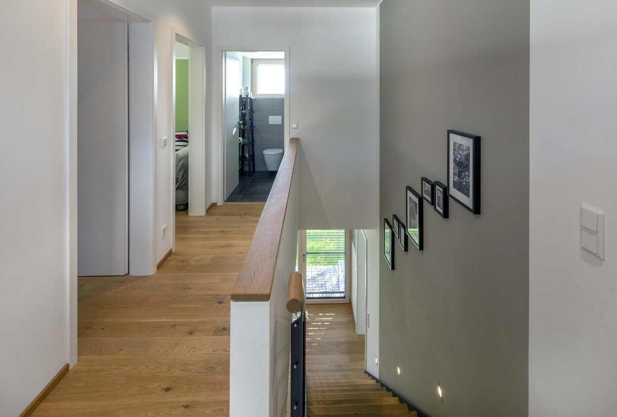 Ein heller Flur in einem Niedrigenergiehaus in Tuntenhausen zeigt Holzboden, eine Treppe und stilvolle Wandbilder.