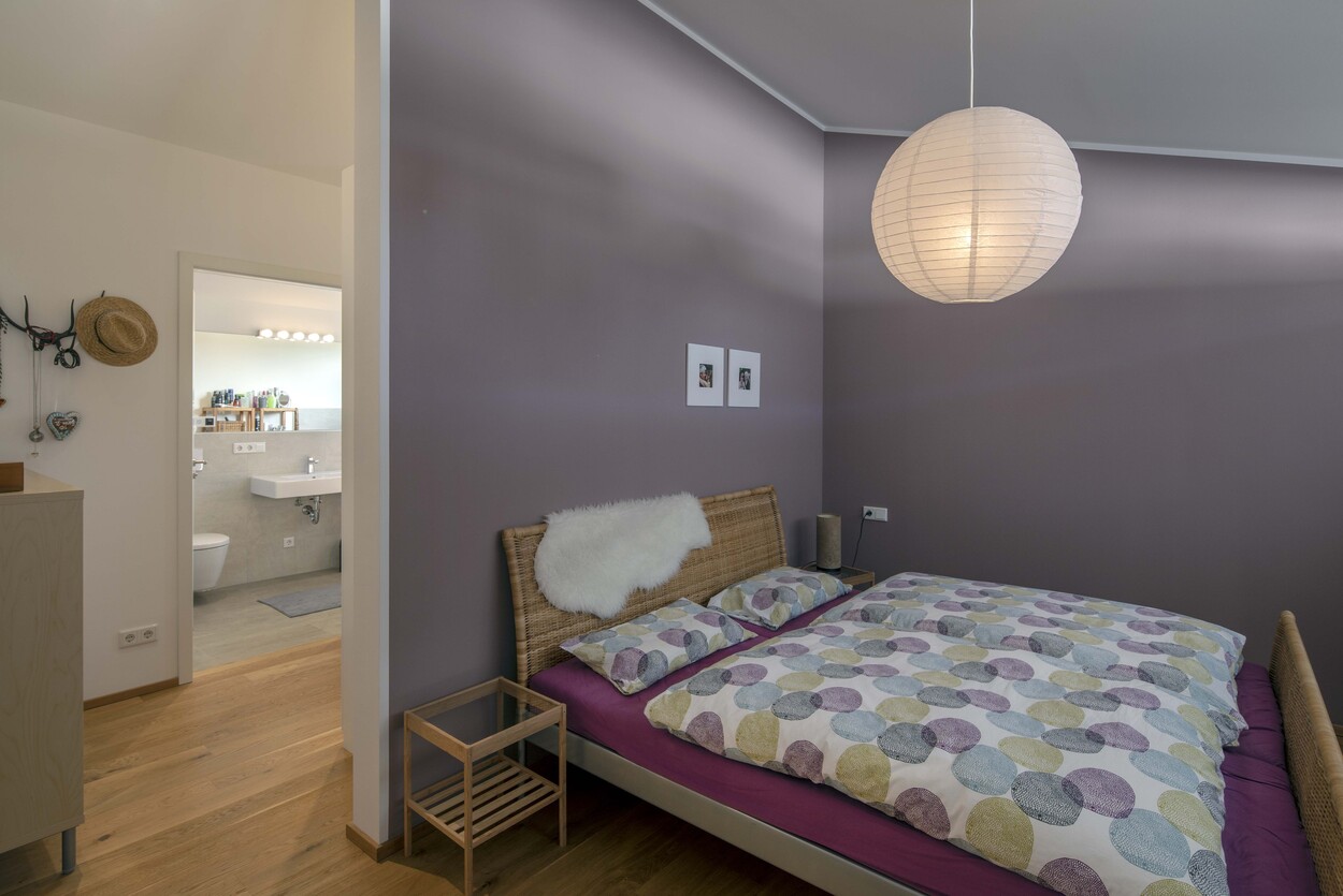 Ein stilvolles Schlafzimmer in einem Niedrigenergiehaus in Tuntenhausen zeigt ein Bett mit bunter Bettwäsche und moderne Lampe.