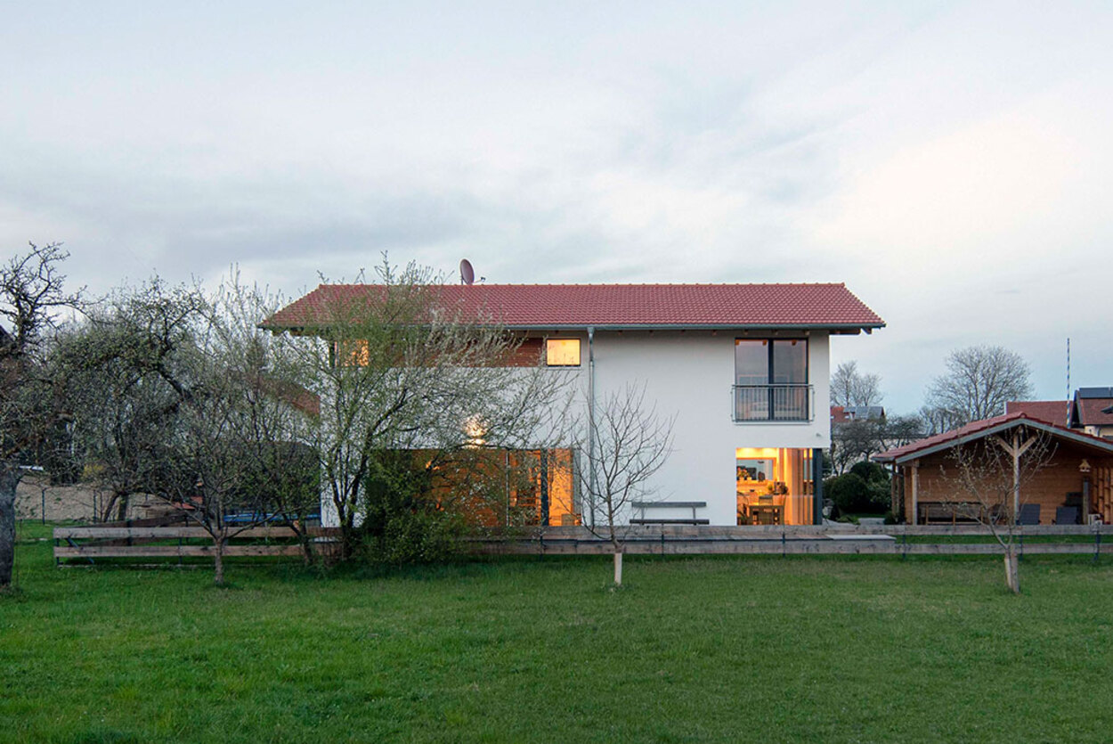 Ein modernes Niedrigenergiehaus mit rotem Dach steht in Tuntenhausen, umgeben von einer grünen, ländlichen Landschaft.